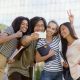 Picture of multiethnic group of young happy students standing and make selfie outdoors. Looking aside.