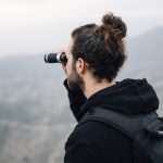 male-hiker-with-his-backpack-looking-mountain-view-through-binocular