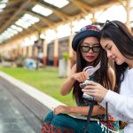 Two happy women are taking pictures while traveling at the train station. Tourism concept